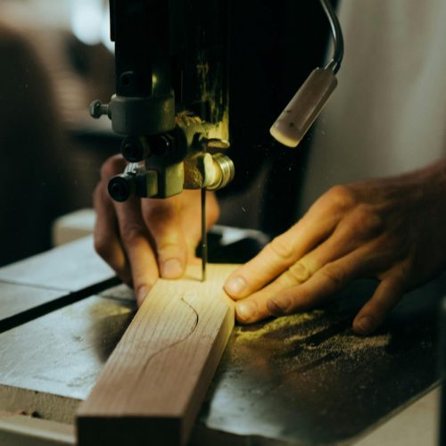 Close-up of a craftsman using a bandsaw to cut wood in a workshop setting.